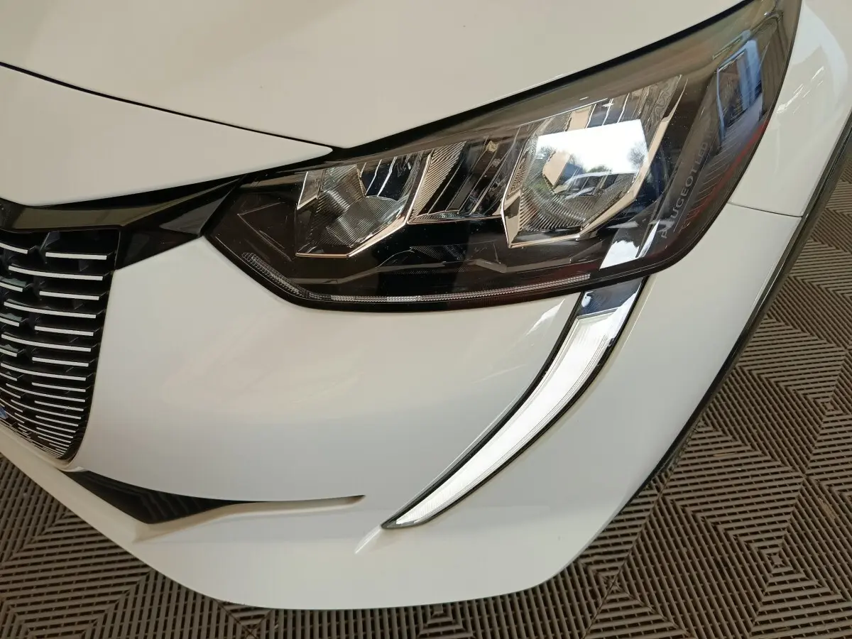 Gros plan sur le phare avant droit blanc de la Peugeot 208 électrique avec signature lumineuse LED distinctive.