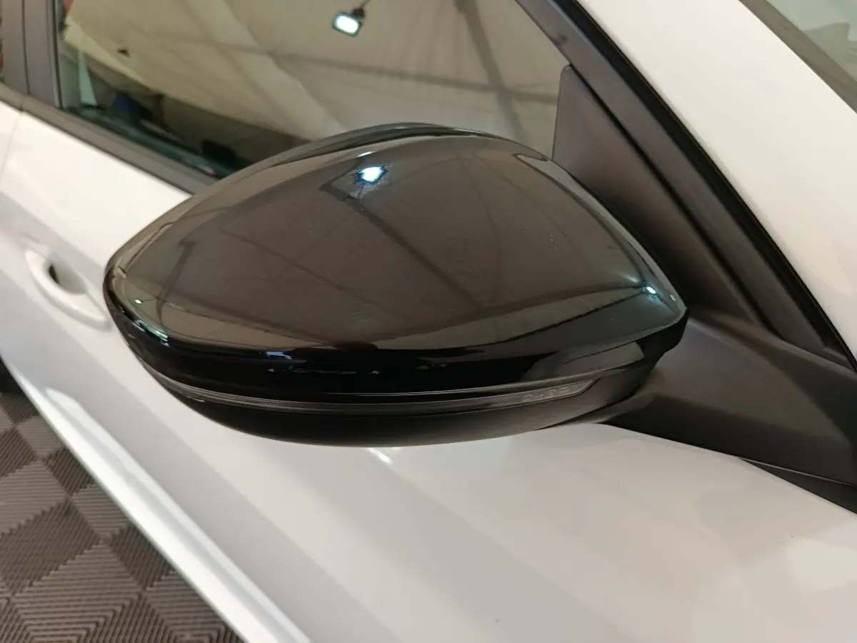 Rétroviseur noir côté gauche sur Peugeot 208 électrique blanche, vue rapprochée en intérieur.