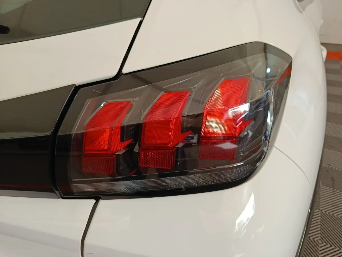 Gros plan sur le feu arrière droit rouge et noir de la Peugeot 208 électrique blanche, version Active Business R.