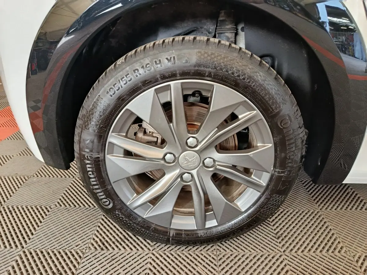 Gros plan sur la roue avant gauche de la Peugeot 208 électrique blanche, avec jante alliage et pneu Continental.