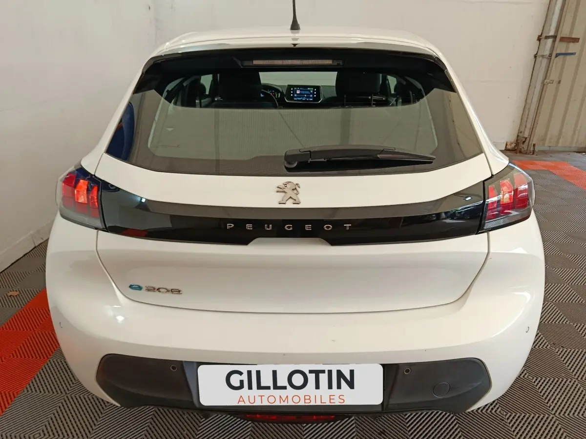 Vue arrière d'une Peugeot 208 électrique blanche avec logo et bande noire distinctive sur le hayon.