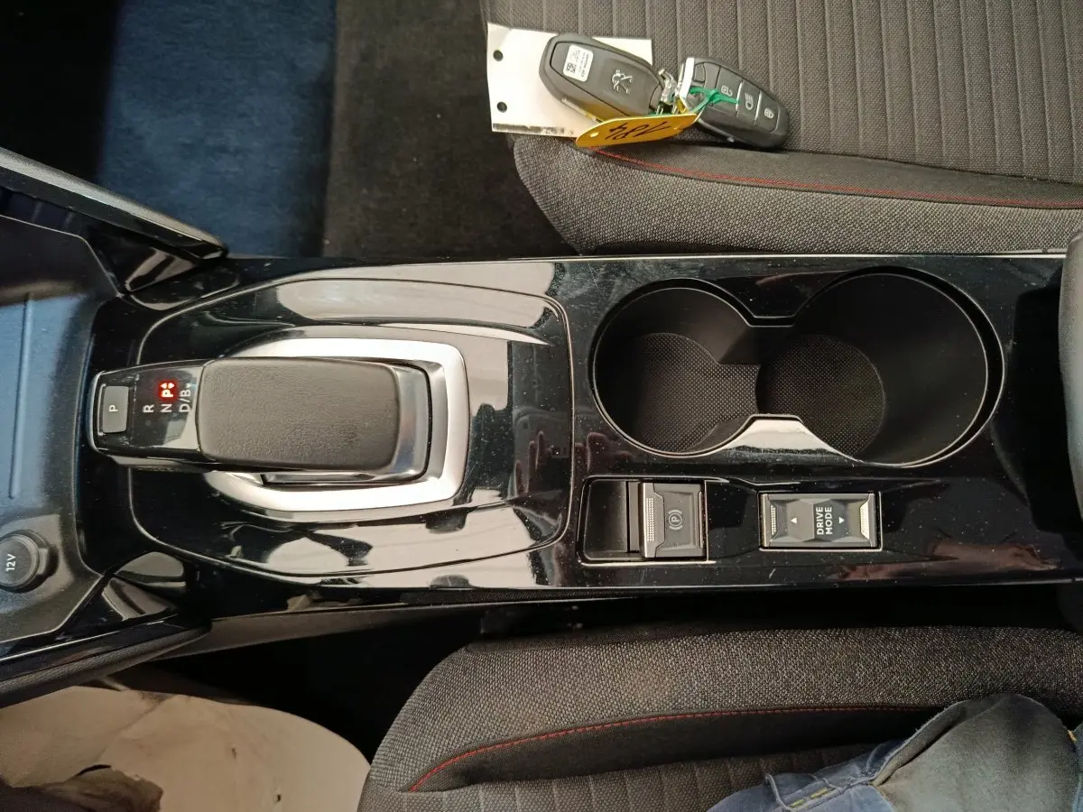 Vue plongeante sur la console centrale noire de la Peugeot 208 électrique avec levier de vitesses et clés posées sur siège gris.