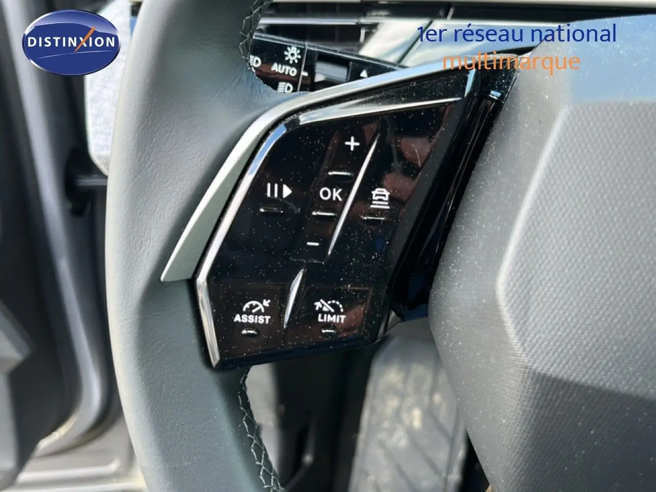 Gros plan sur les commandes noires du volant cuir gris du Peugeot 5008 Hybrid 2025, avec boutons d’assistance et limitation.