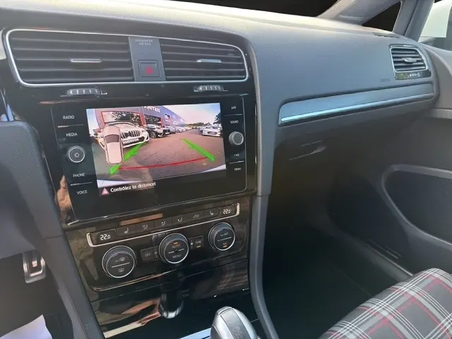 Vue intérieure centrée sur la console centrale d'une Volkswagen Golf GTI Performance blanche, avec écran tactile et levier de vitesse.
