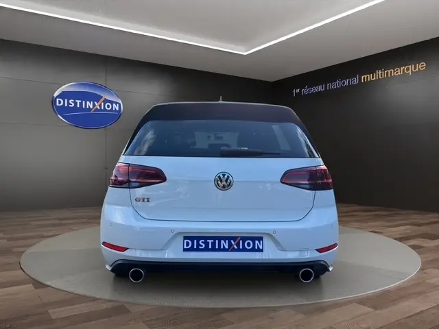 Vue 3/4 arrière droite d’une Volkswagen Golf GTI Performance blanche, avec jantes noires et feux arrière teintés.