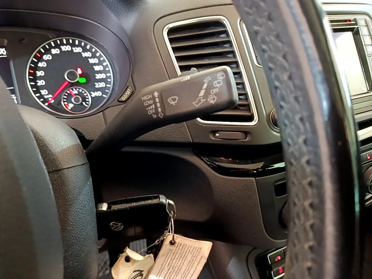 Gros plan intérieur sur le volant cuir et la commande d’essuie-glace du Volkswagen Sharan 2017, tableau de bord noir.