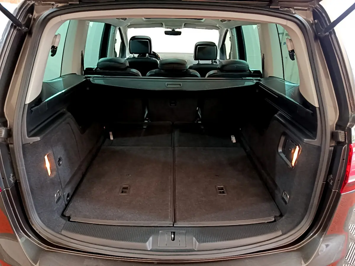 Coffre ouvert vu de l'arrière d'un Volkswagen Sharan marron, montrant un grand espace de chargement plat et les sièges arrière.