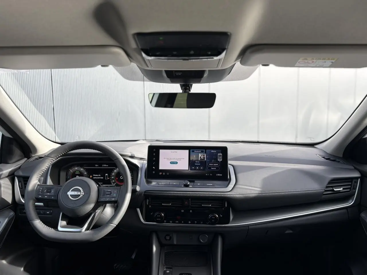 Vue frontale intérieure du Nissan Qashqai blanc nacré 2025, tableau de bord moderne avec écran tactile central et volant multifonction.