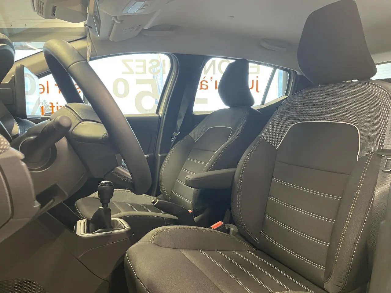 Vue intérieure côté conducteur de la Dacia Sandero Stepway 2025, sièges tissu noirs avec accoudoir central.