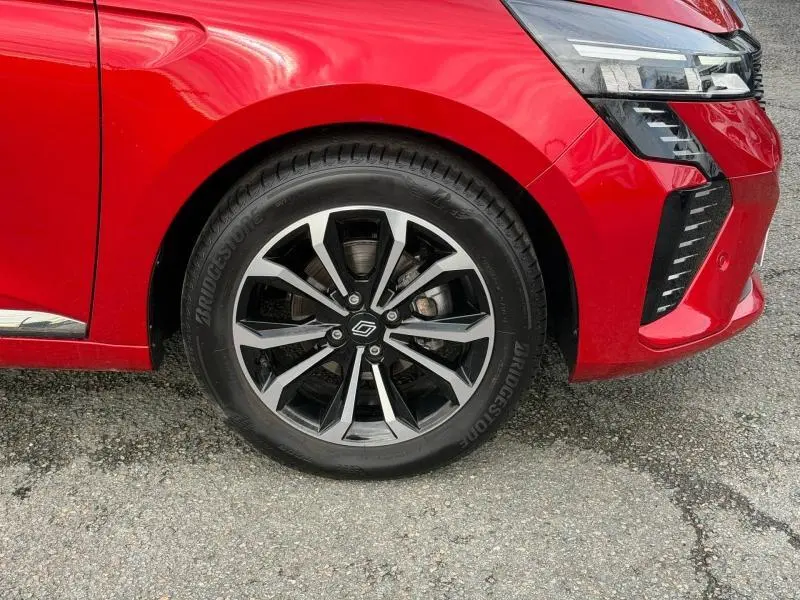 Gros plan sur la roue avant gauche et le pare-chocs avant rouge flamme d'une Renault Clio 1.0 TCe 90ch Techno 2025.