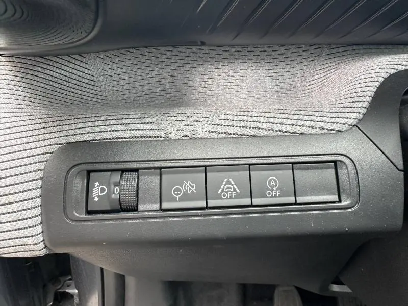 Gros plan sur les commandes de réglage des phares et aides à la conduite dans une Citroën C3 1.2 Turbo 100ch MAX, intérieur gris.