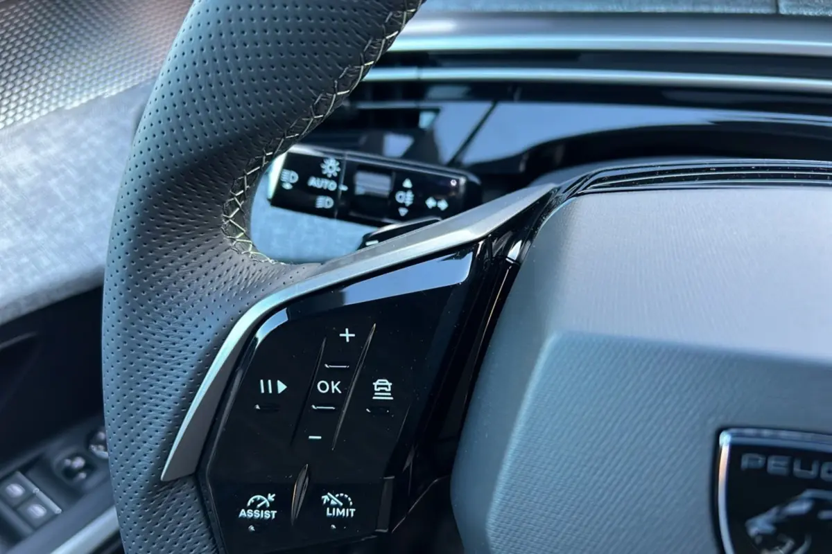 Gros plan sur le volant cuir perforé du Peugeot 3008 Hybrid 145 GT, avec commandes multifonctions et palettes aluminium.
