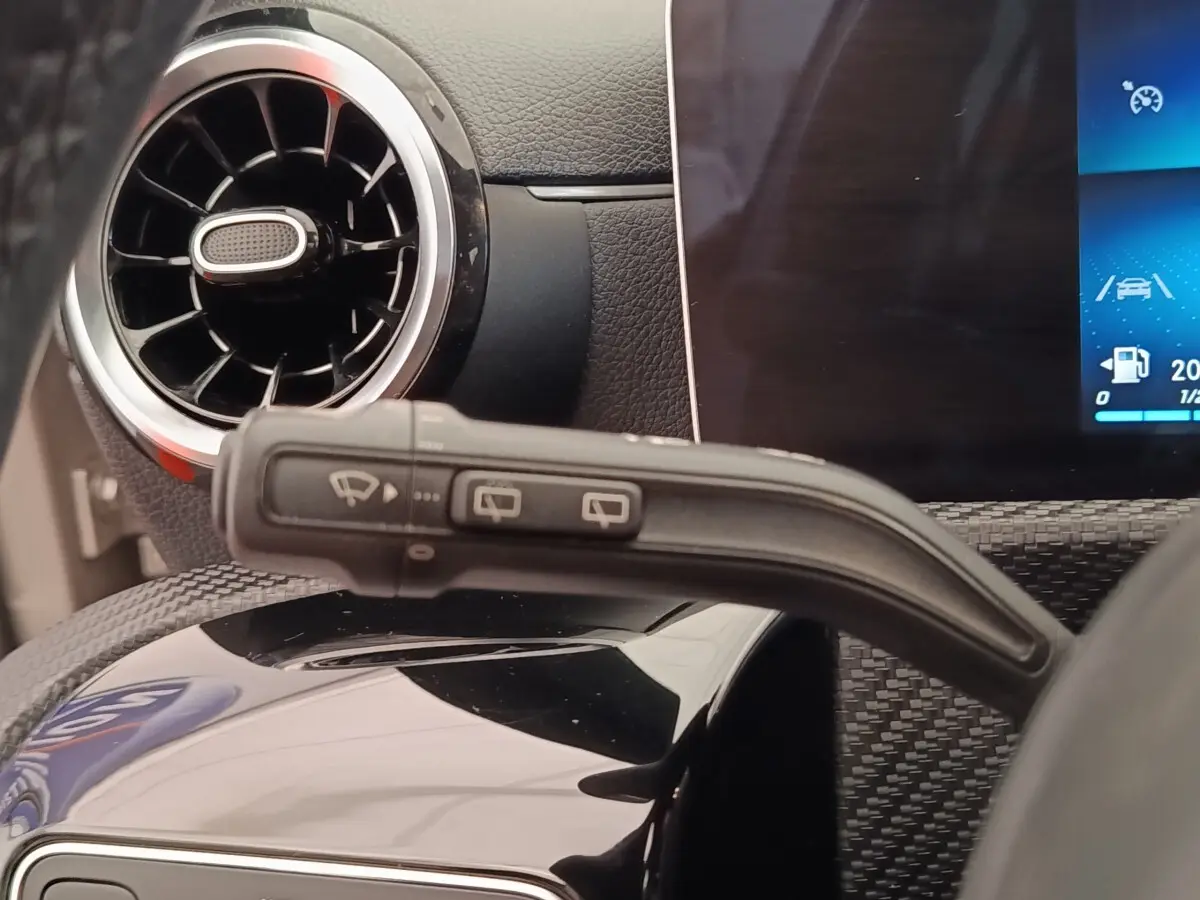 Détail intérieur du levier d’essuie-glace avec aérateur rond et écran tactile du tableau de bord d’une Mercedes Classe A gris clair.
