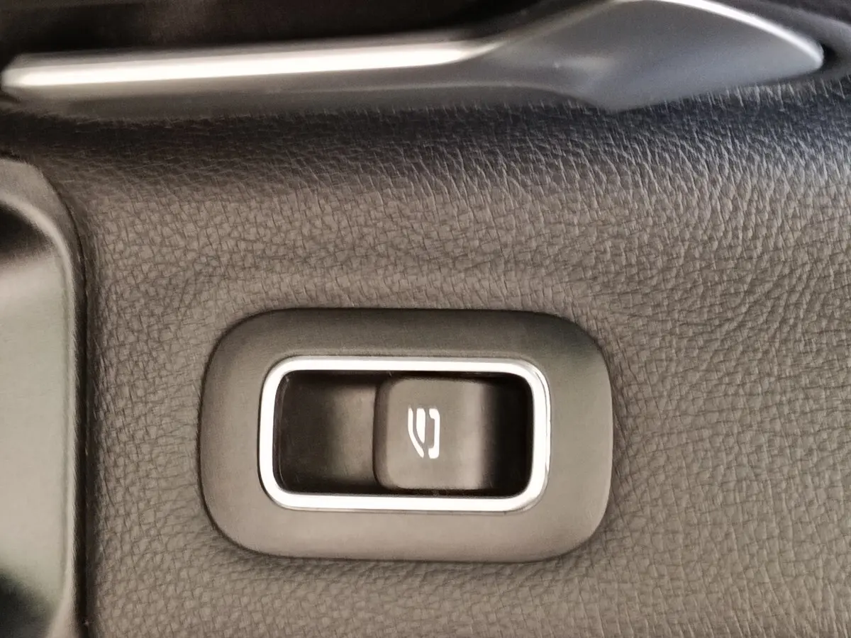 Gros plan sur le bouton d'ouverture du coffre intégré dans le revêtement noir texturé intérieur d'une Mercedes Classe A gris clair.