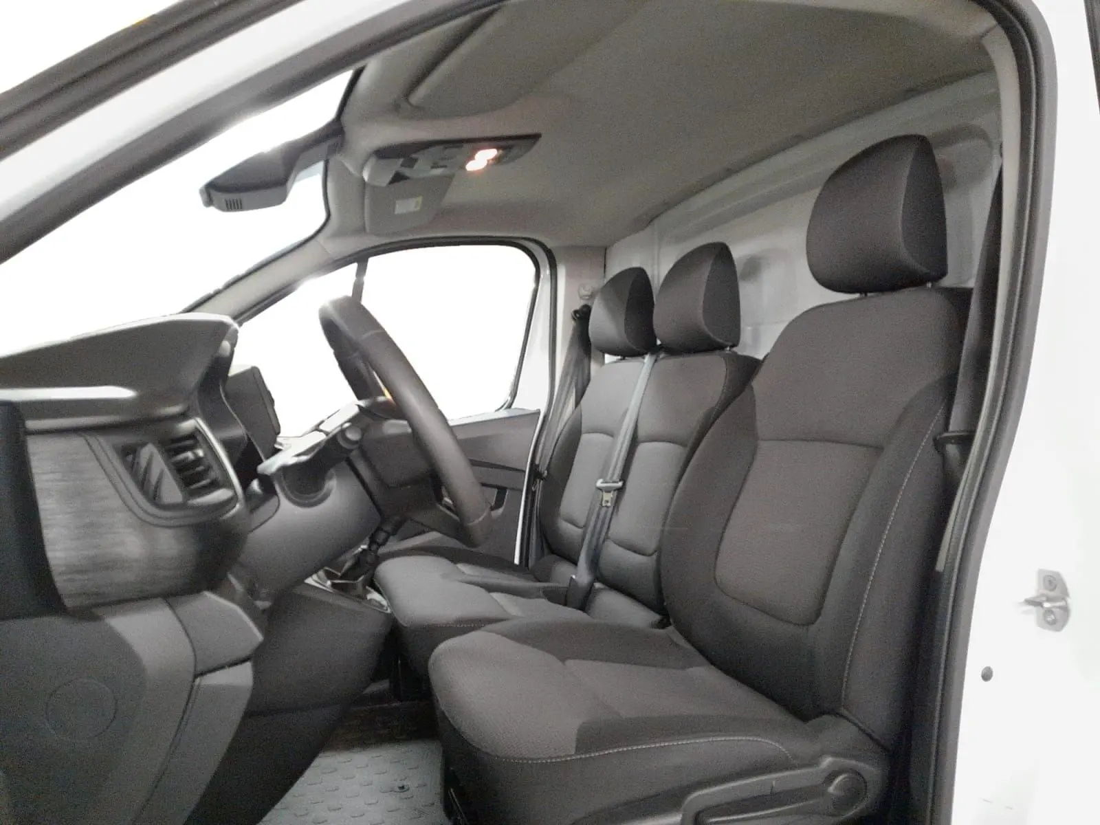 Vue intérieure côté conducteur du Renault Trafic Fourgon 2024 blanc, montrant les sièges tissu noirs et le tableau de bord.