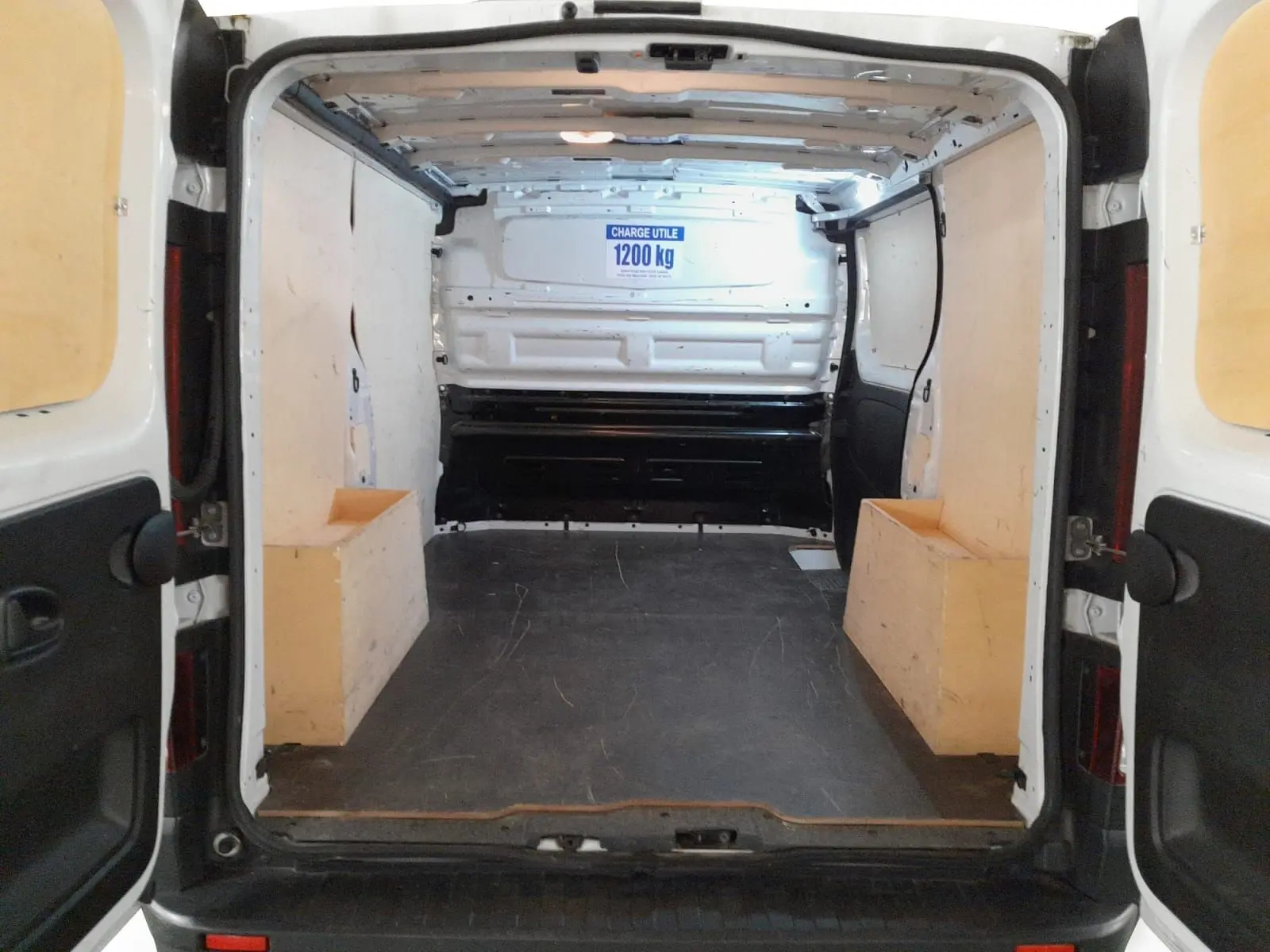 Vue arrière intérieure du Renault Trafic Fourgon blanc minéral 2024, montrant l’espace de chargement vide avec panneaux bois.