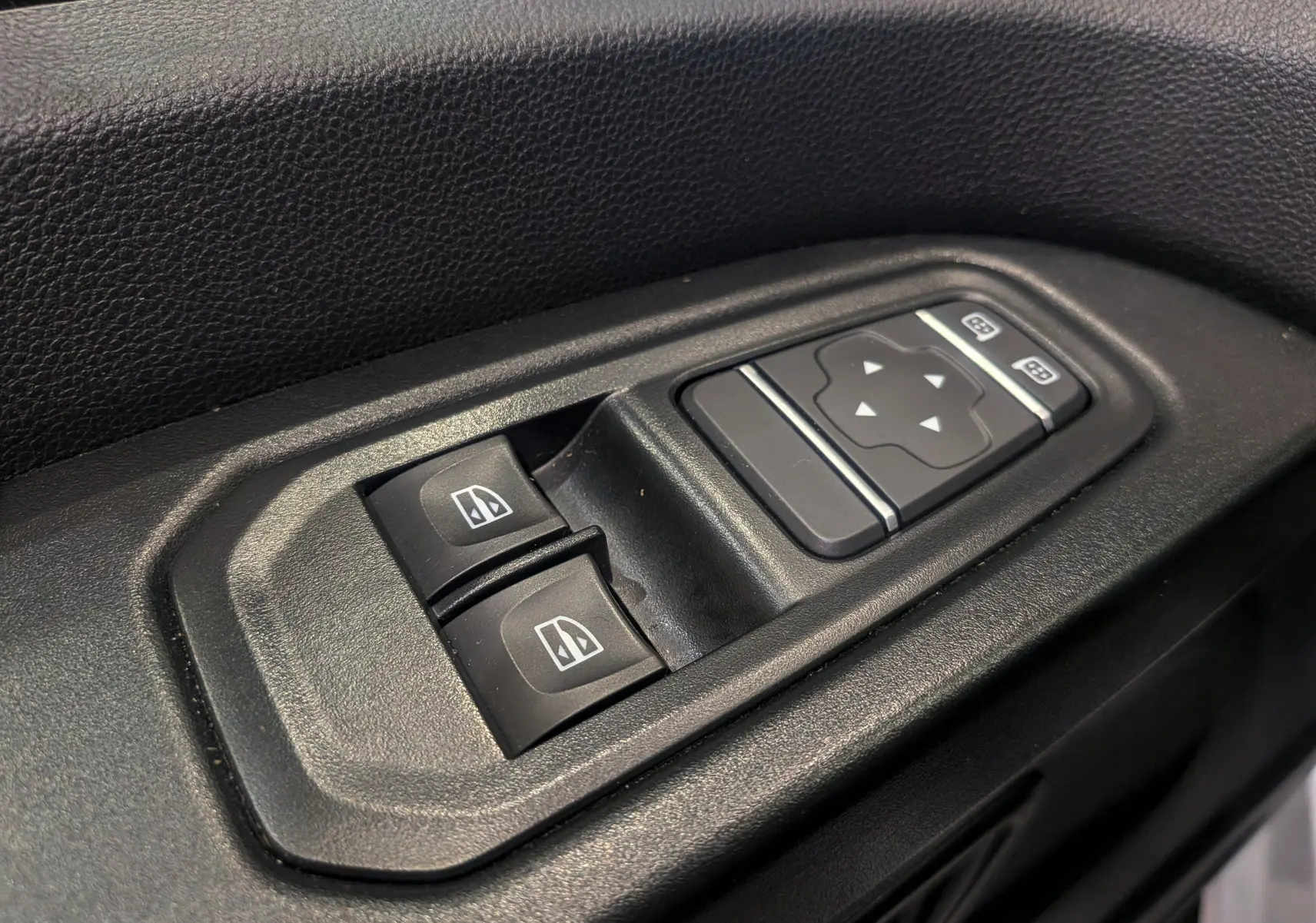 Gros plan sur les commandes de lève-vitres et réglage des rétroviseurs côté conducteur du Renault Trafic Fourgon blanc 2024.