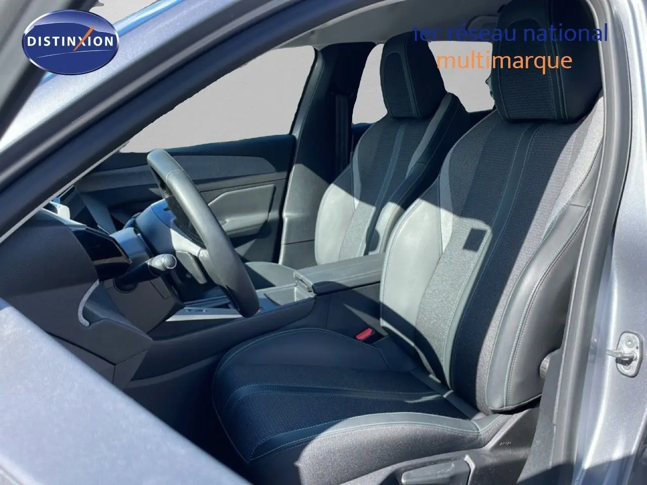 Vue intérieure côté conducteur de la Peugeot 308 SW Hybrid 2025, sièges tissu et cuir gris noir, volant multifonction.