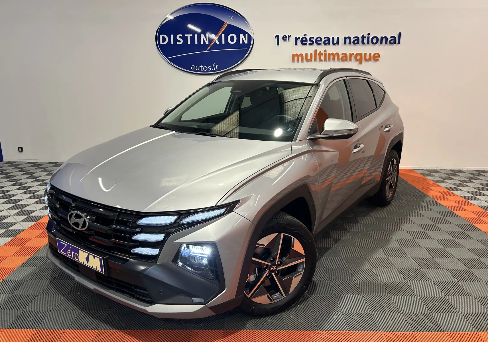 Hyundai Tucson 2025 hybride en Shimmering Silver, vue 3/4 avant droit avec jantes 18 pouces et phares allumés.