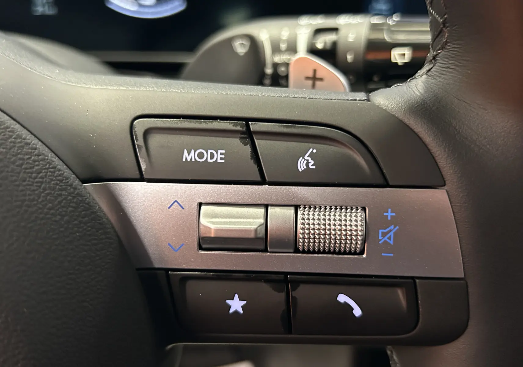 Gros plan sur les commandes gauche du volant du Hyundai Tucson 2025 en cuir noir avec molette et boutons rétroéclairés.