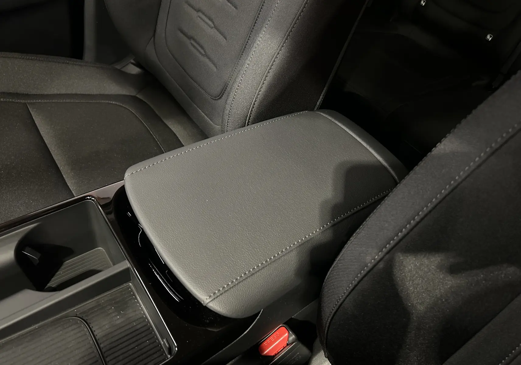 Gros plan sur l'accoudoir central en cuir gris et les sièges tissu noirs à l'avant du Hyundai Tucson 2025.