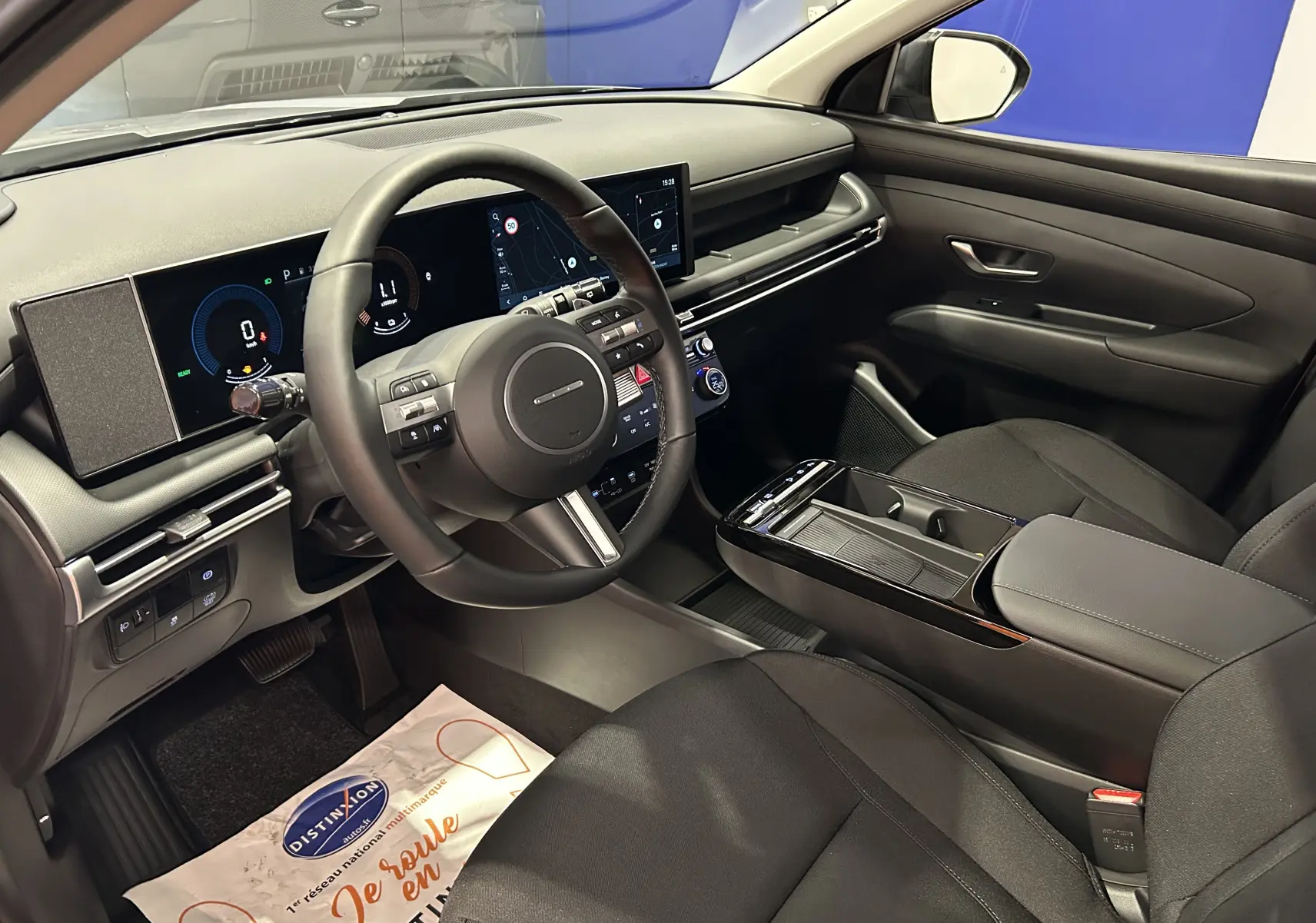 Intérieur du Hyundai Tucson 2025, vue côté conducteur, tableau de bord numérique et sièges tissu noirs visibles.