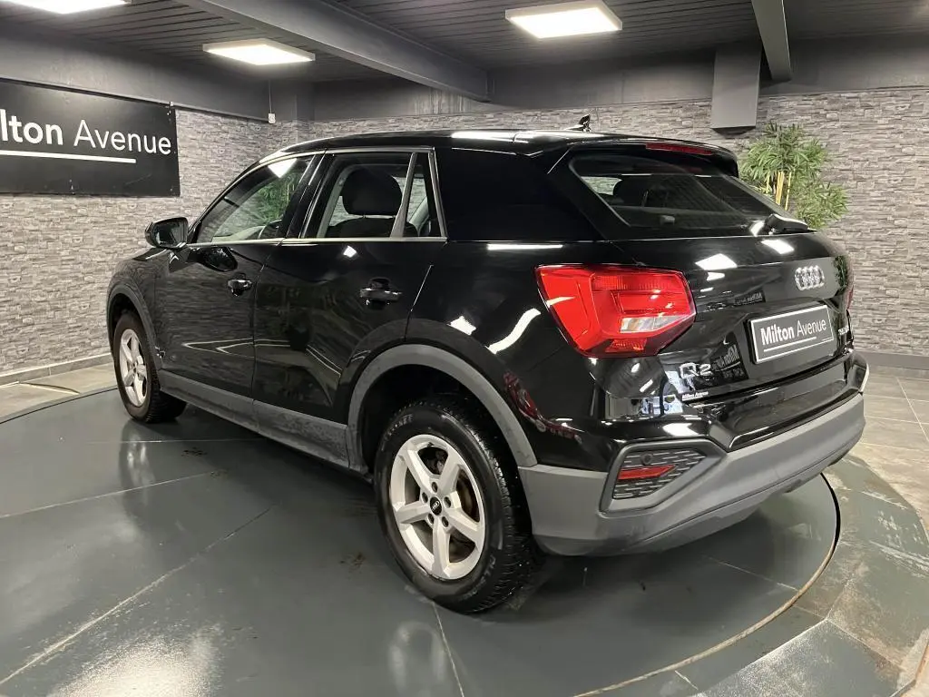 Audi Q2 noir brillant vue 3/4 arrière droit, avec feux LED et jantes aluminium 16 pouces dans showroom.