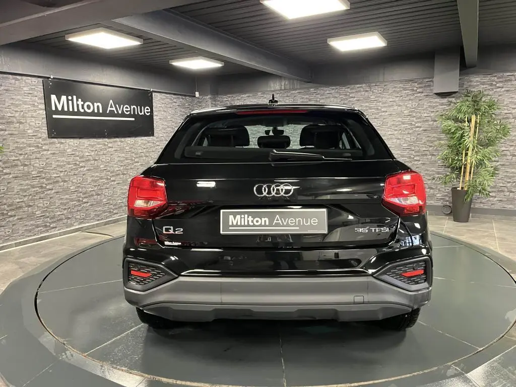 Vue arrière d'un Audi Q2 noir brillant 2022 avec feux LED et logo distinctif sur fond intérieur showroom.