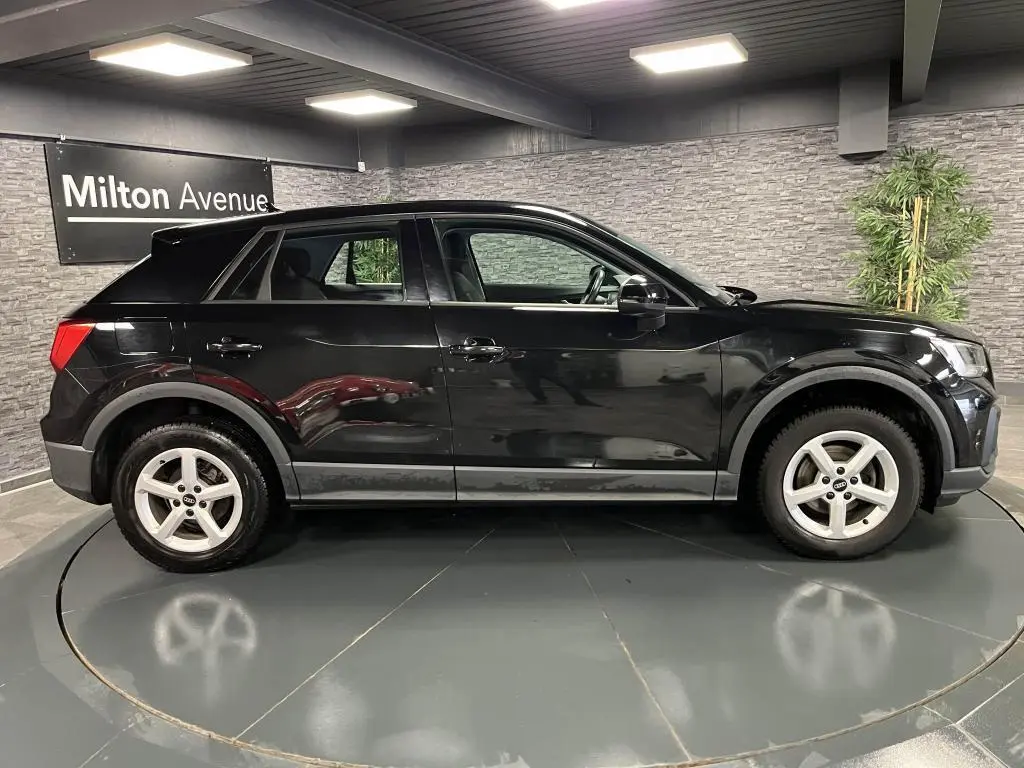 Audi Q2 noir vue de profil côté gauche dans un showroom avec jantes aluminium 16 pouces et peinture vernie brillante.