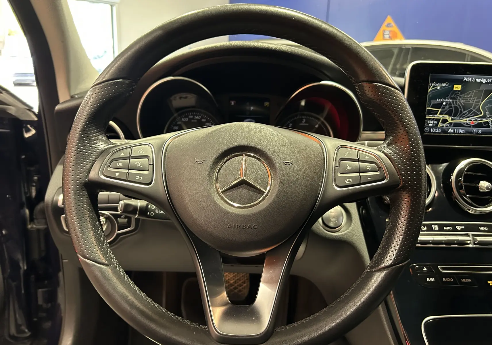 Vue rapprochée du volant en cuir perforé d'une Mercedes Classe C 200d 2018 avec écran GPS allumé à droite.