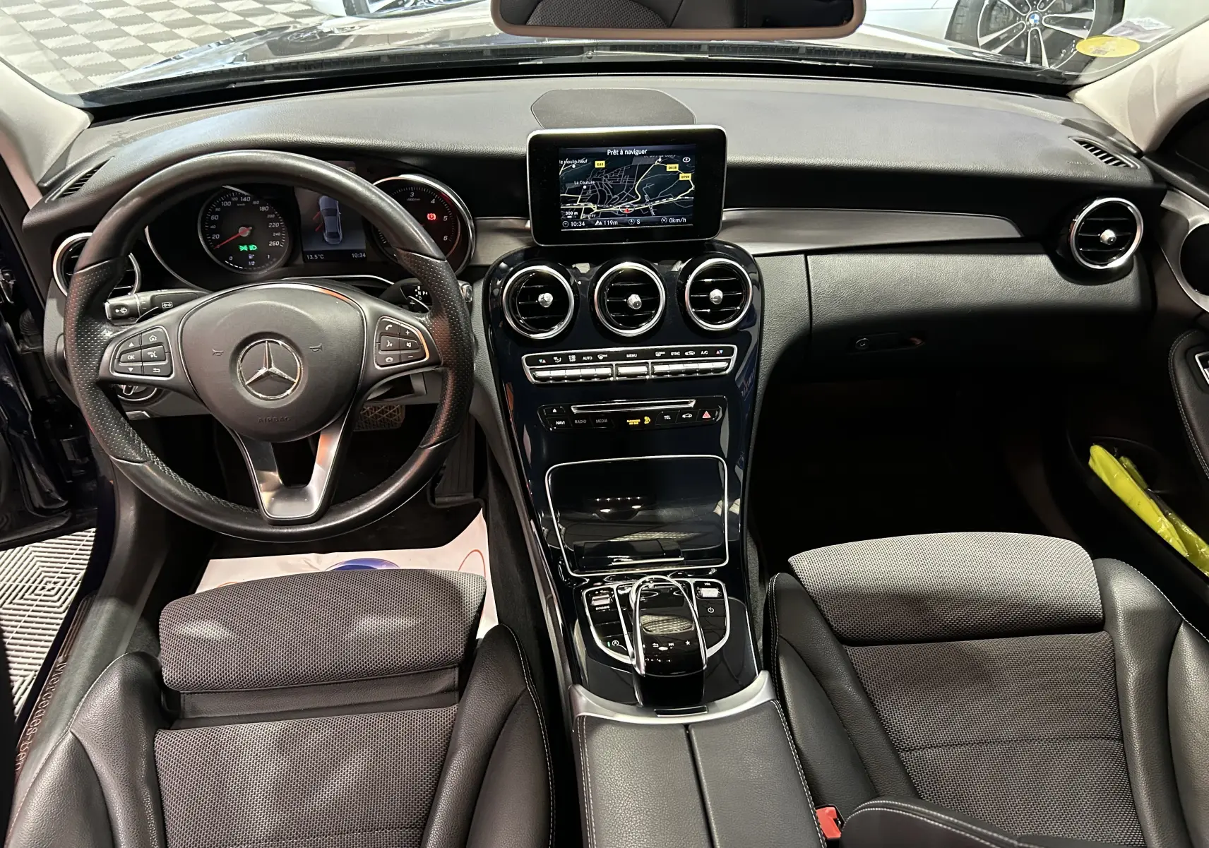 Vue intérieure avant de la Mercedes Classe C 200d bleu, mettant en valeur le tableau de bord et l'écran GPS central.