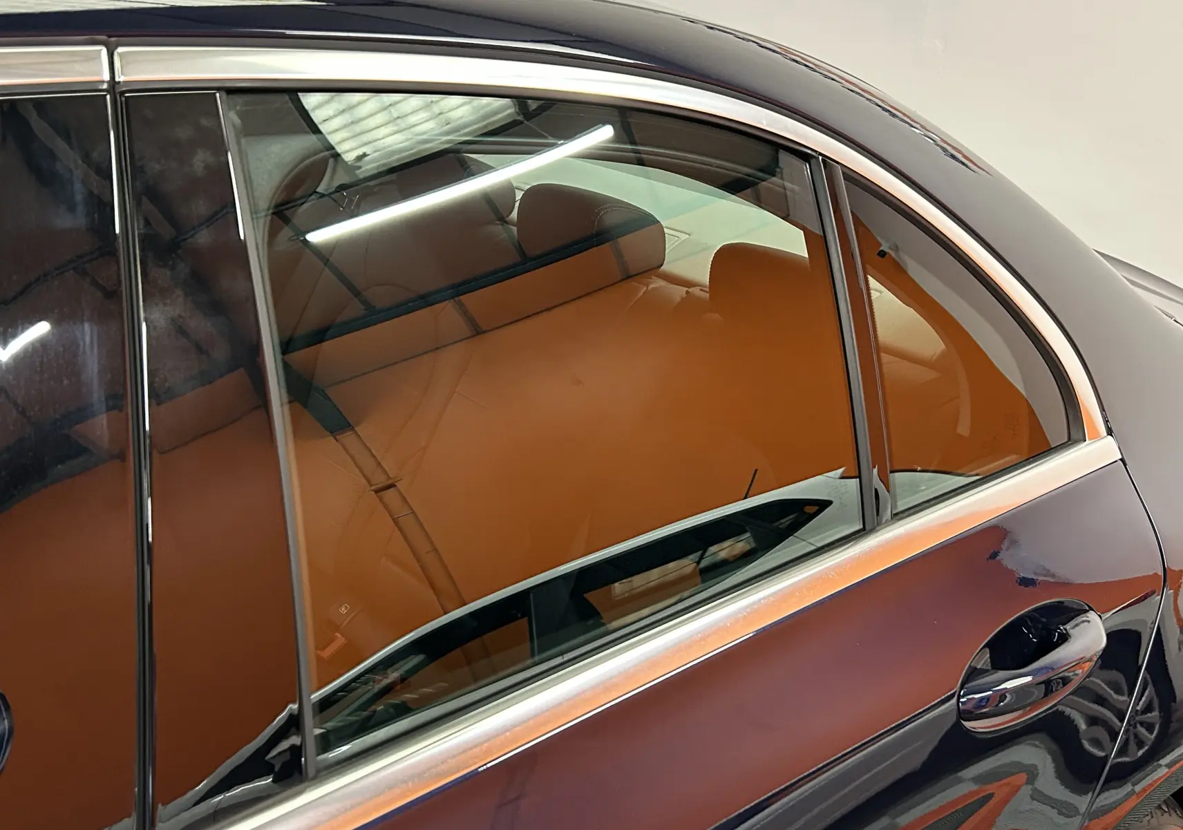 Vue latérale côté droit d'une Mercedes Classe C 200d bleu avec intérieur cuir marron visible à travers la vitre arrière.