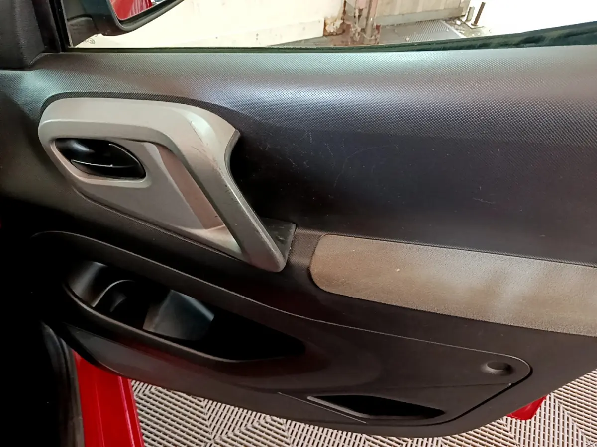 Gros plan sur la porte intérieure côté conducteur du Citroën Berlingo rouge 2016, avec poignée grise et panneau noir.