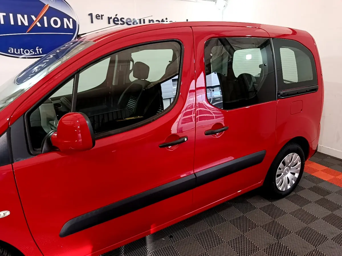 Profil côté gauche du Citroën Berlingo rouge 2016 avec portes vitrées et rétroviseurs assortis en intérieur showroom.