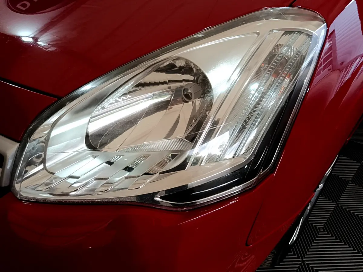 Gros plan sur le phare avant droit du Citroën Berlingo rouge, mettant en valeur son design et la carrosserie brillante.