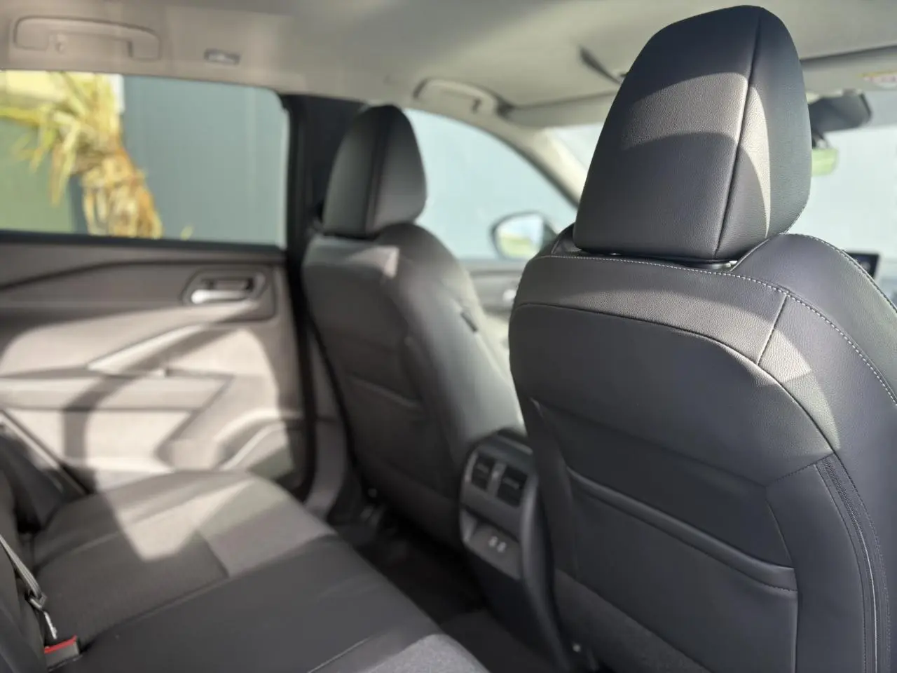 Vue intérieure arrière côté gauche du Nissan Qashqai blanc nacré, montrant les sièges avant en cuir noir et les aérateurs arrière.