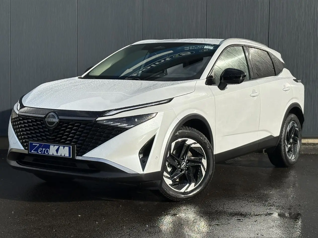 Nissan Qashqai blanc nacré en 3/4 avant droit, avec calandre noire texturée et jantes alliage noires.