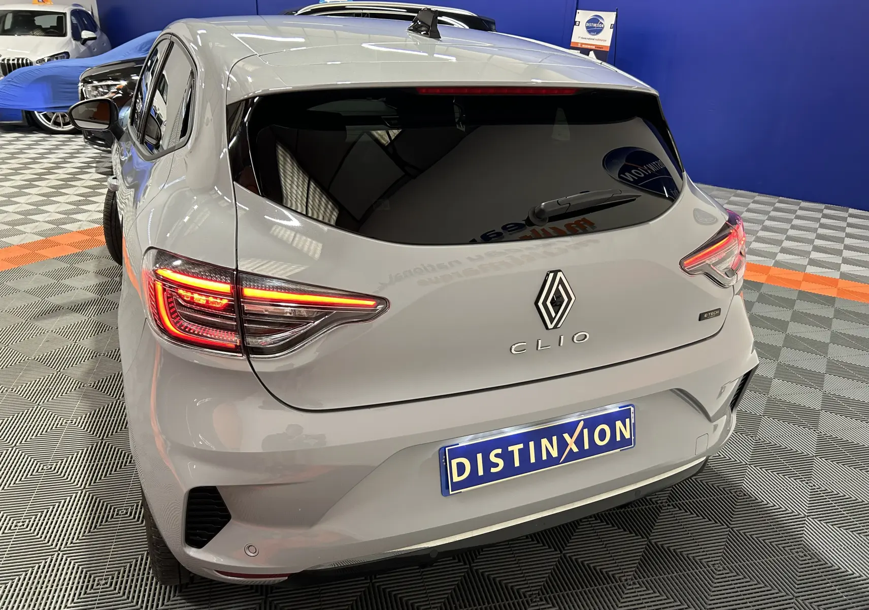 Vue 3/4 arrière droite d'une Renault Clio V E-Tech gris Rafale métal avec feux arrière allumés en intérieur showroom.