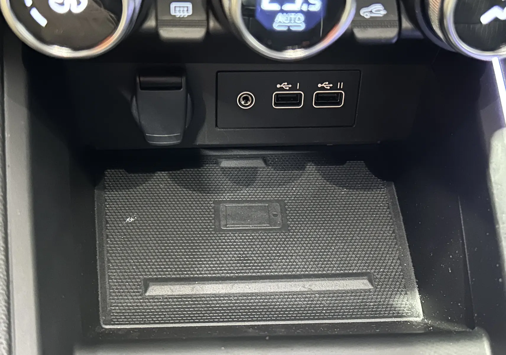 Gros plan sur la console centrale de la Renault Clio V E-Tech, montrant les ports USB et la zone de recharge sans fil.