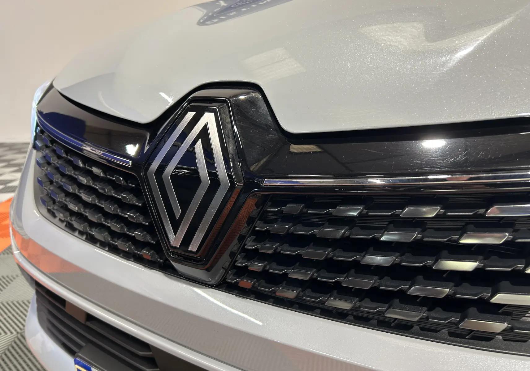 Gros plan sur la calandre avant gris rafale métal de la Renault Clio V E-Tech avec logo Renault chromé central.