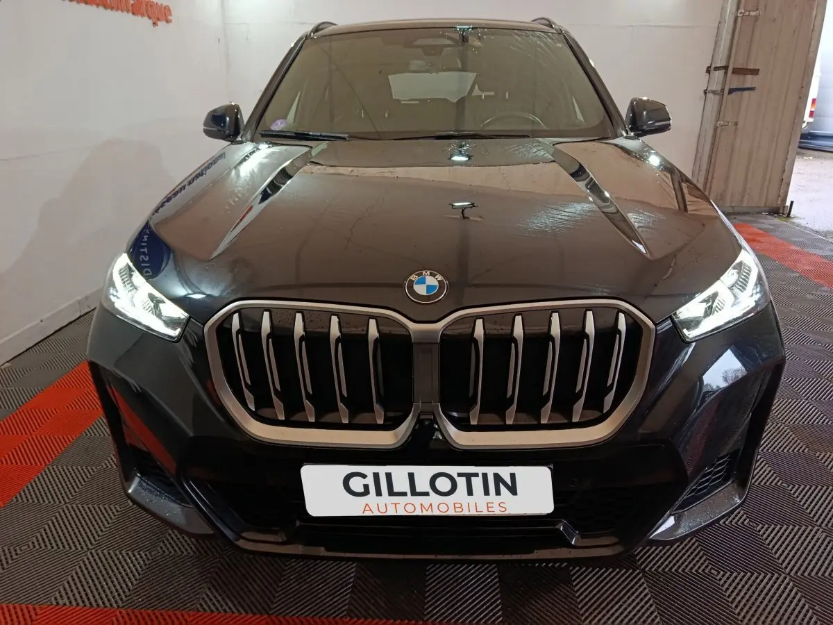 Vue avant rapprochée d’un BMW X1 noir avec calandre imposante et phares LED allumés dans un garage.