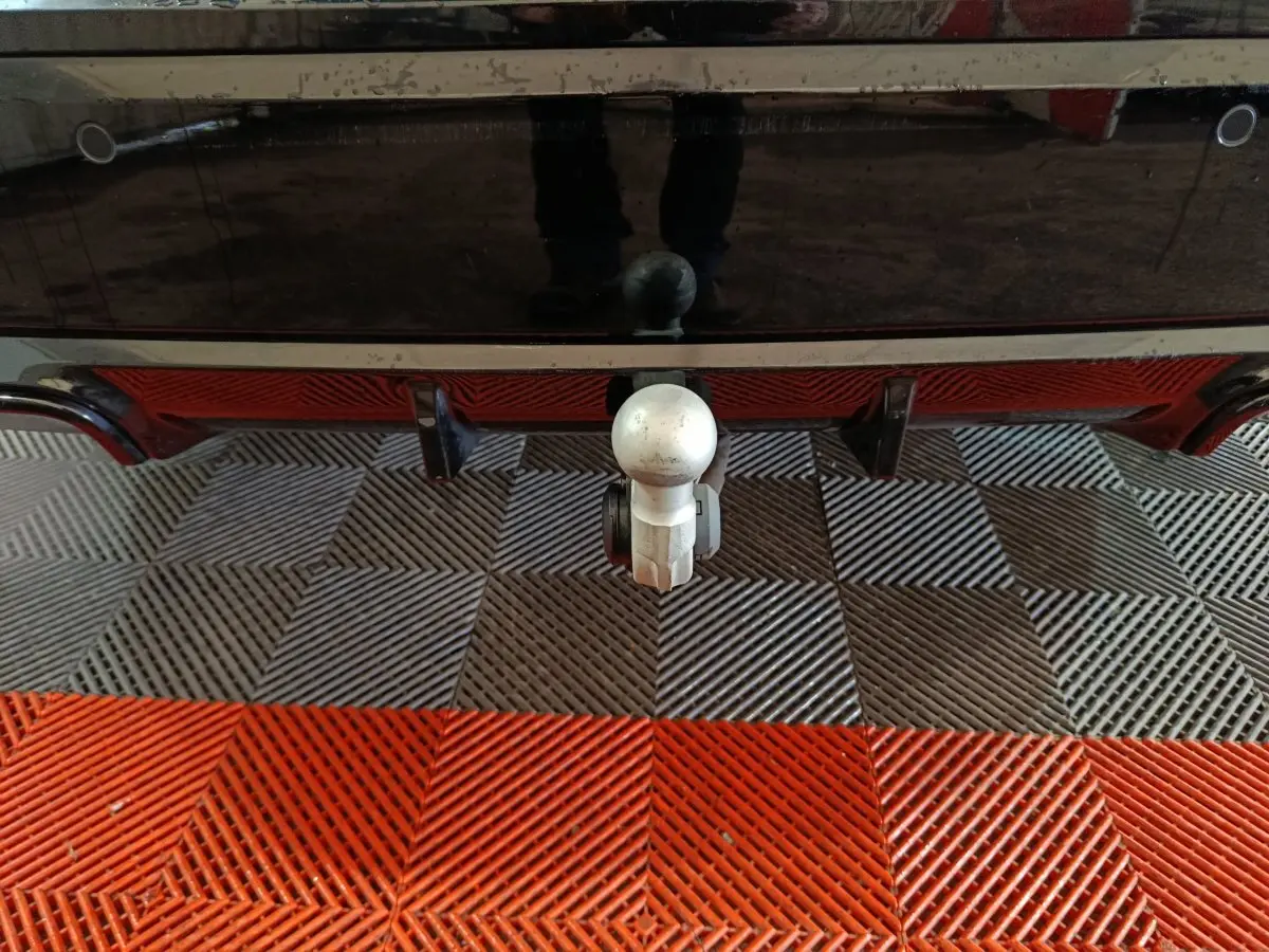 Gros plan sur l'attelage arrière d'un BMW X1 noir, mettant en valeur la boule d'attelage sur sol carrelé bicolore.