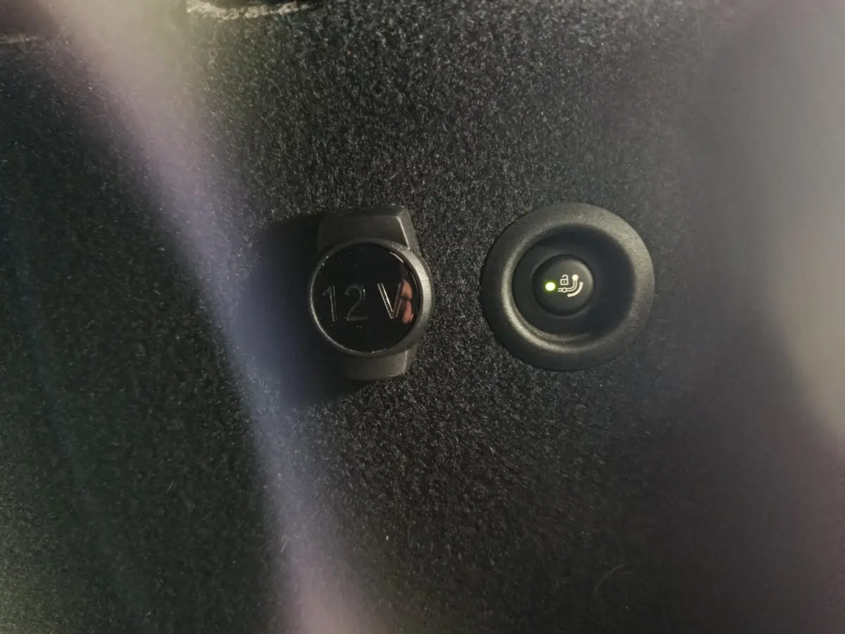 Détail intérieur montrant la prise 12V et le bouton de commande de ventilation additionnelle sur fond noir.