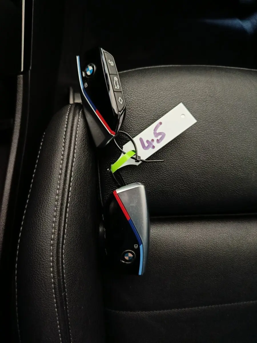 Gros plan sur deux clés BMW noires avec bandes tricolores posées sur un siège en cuir noir.