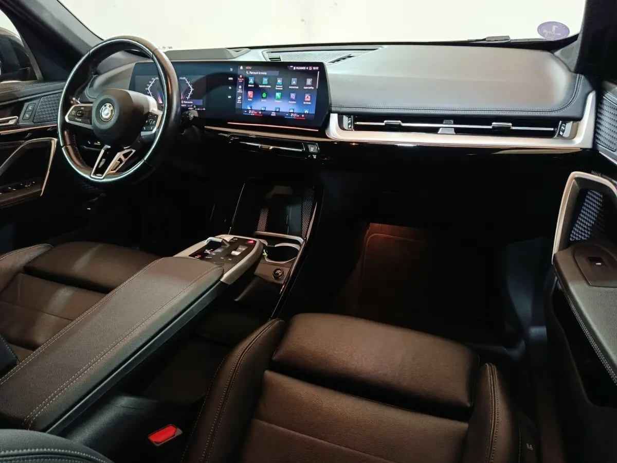 Intérieur noir BMW X1 xDrive23i M Sport 2023, vue de profil droit sur tableau de bord et volant cuir alu multifonctions.