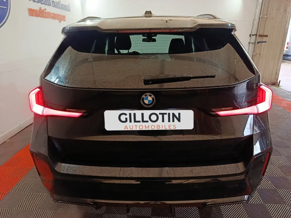 Vue arrière d’un BMW X1 noir avec feux arrière LED allumés dans un garage fermé.