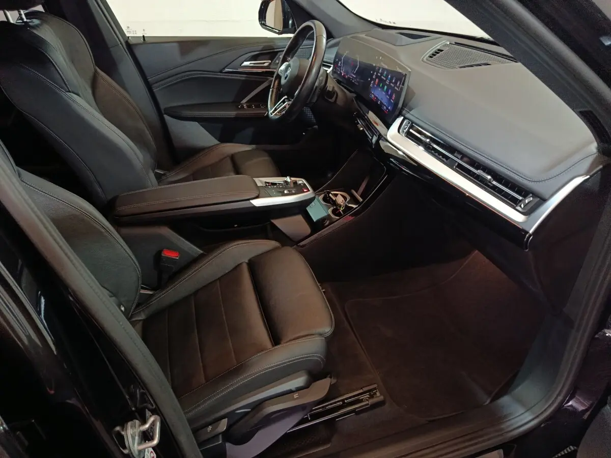Vue intérieure côté conducteur de la BMW X1 xDrive23i M Sport 2023 avec sièges cuir noirs et écran tactile large.
