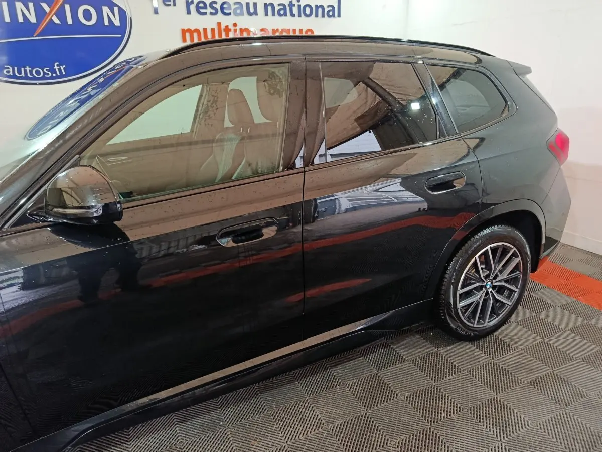 Vue de profil côté droit d'un BMW X1 noir 2023 avec jantes alliage et vitres teintées dans un showroom.
