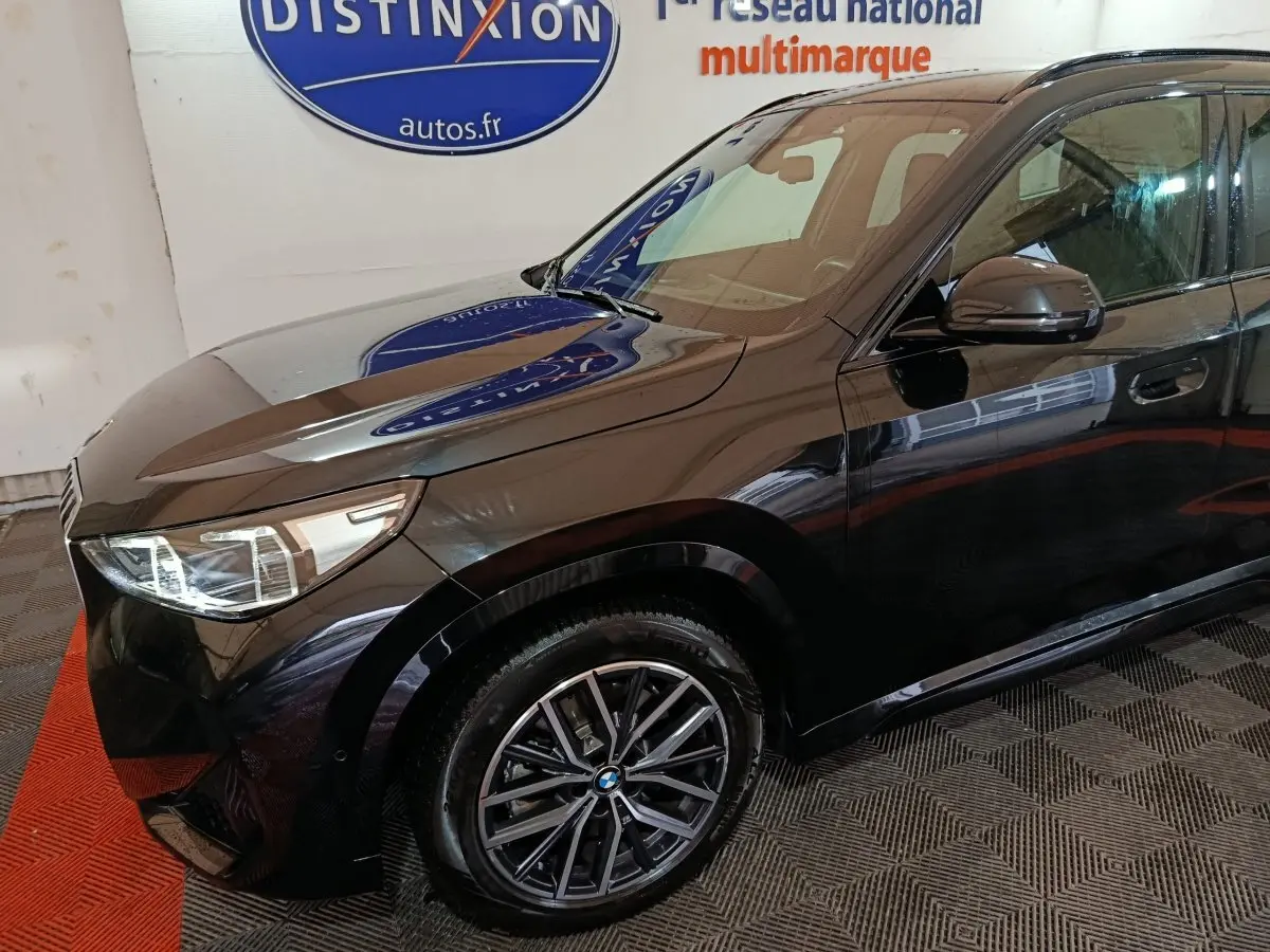 Vue 3/4 avant gauche d’un BMW X1 xDrive23i M Sport noir brillant avec jantes alliage et phares LED visibles.
