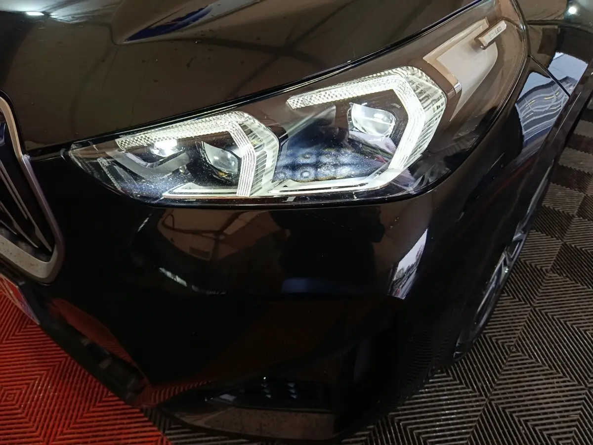Gros plan sur le phare avant droit LED d’un BMW X1 noir xDrive23i M Sport 2023, avec calandre partielle visible.
